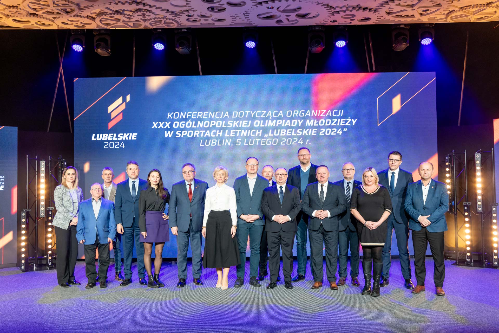 Wszyscyuczestnicy konferencji pozują do wspólnego zdjęcia na okazjonalnej ściance. Łącznie na zdjęciu znajduje się kilkanaście osób.