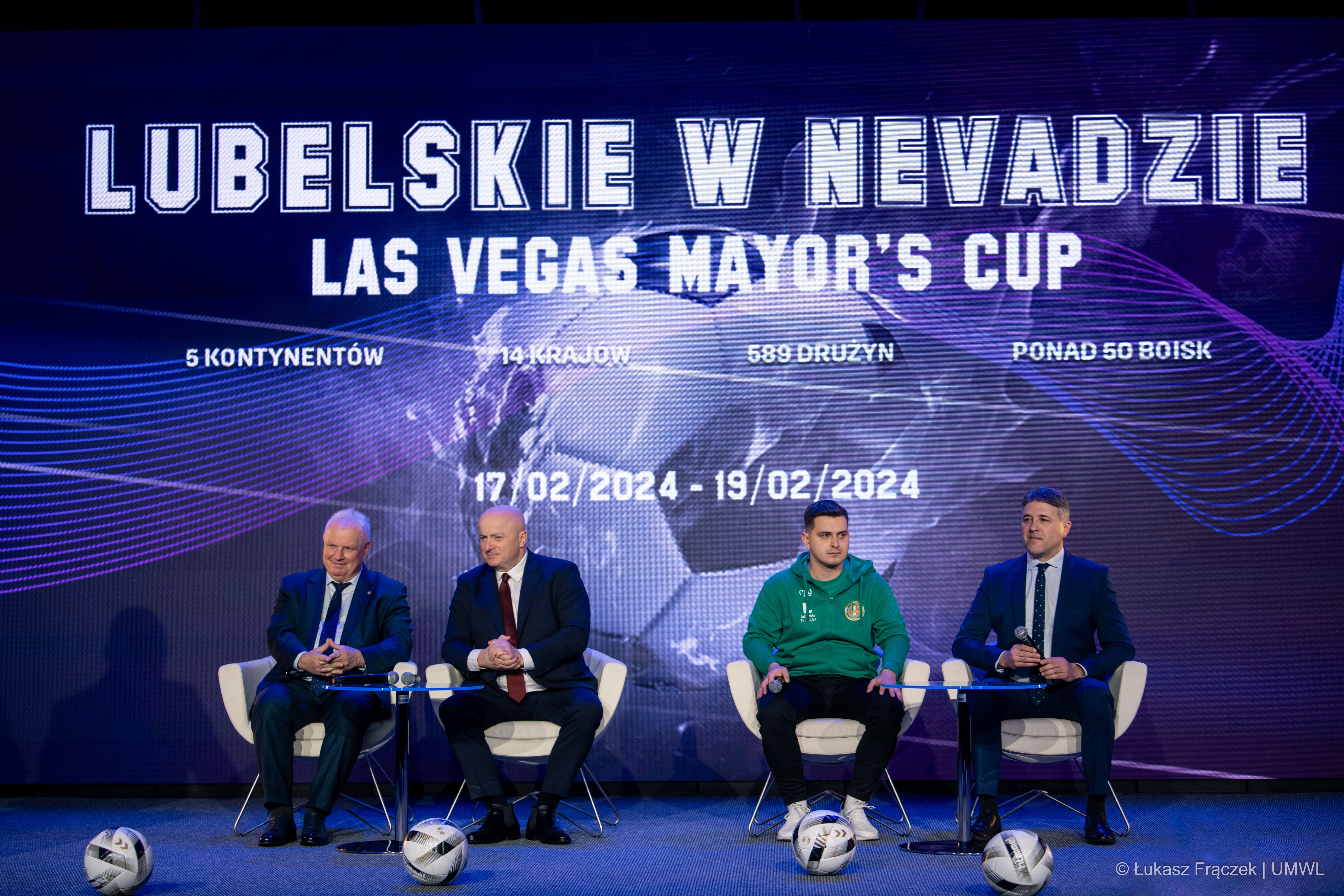 Uczestnicy konferencji czterech mężczyzn siedzi przy stole konferencyjnym, przed każdym z nich leży piłka piłkarska