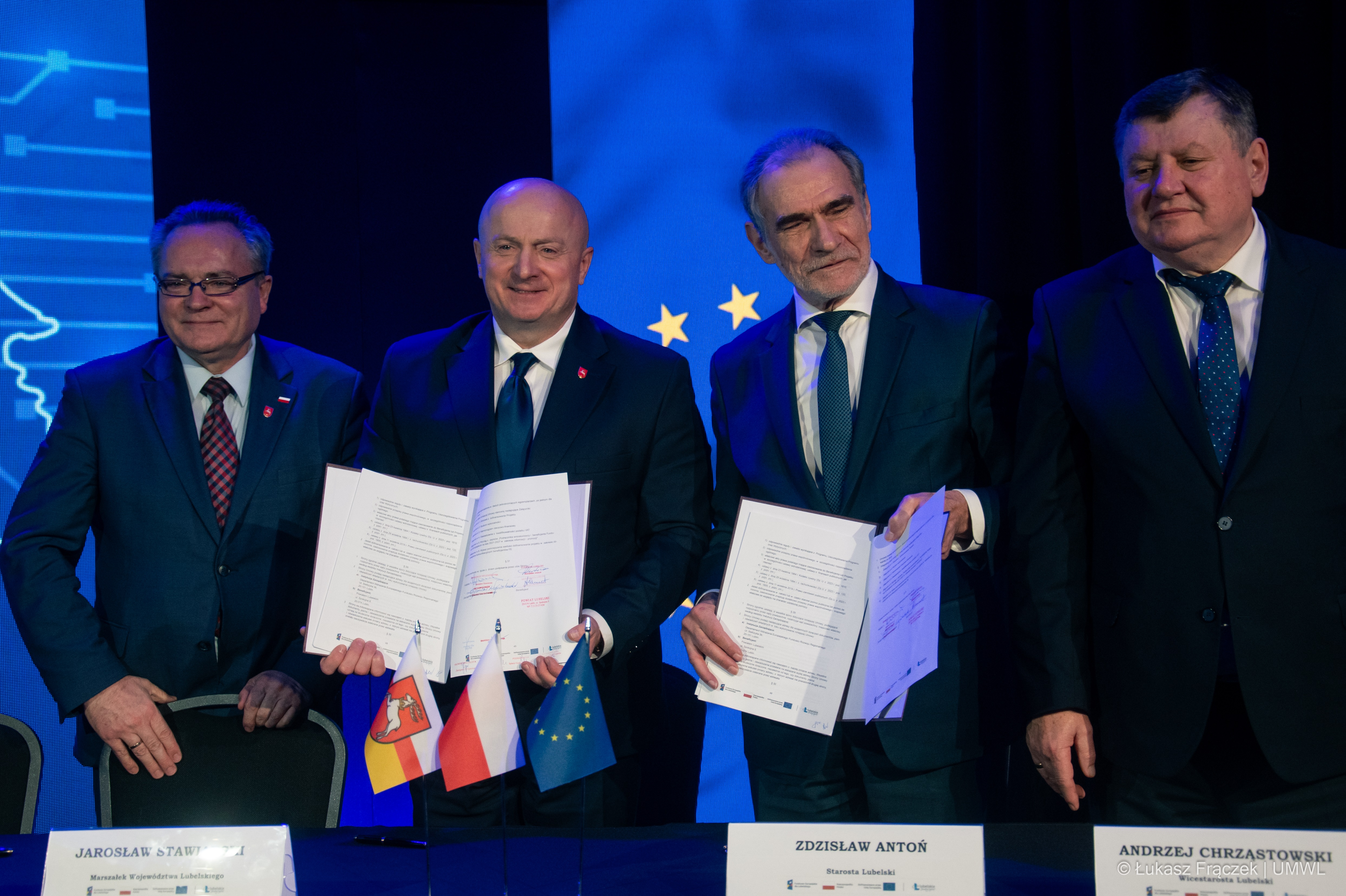 Jarosław Stawiarski i Zdzisław Anton stoją obo siebie w towarzystwie dwóch innych mężczyzn i prezentują podpisane umowy