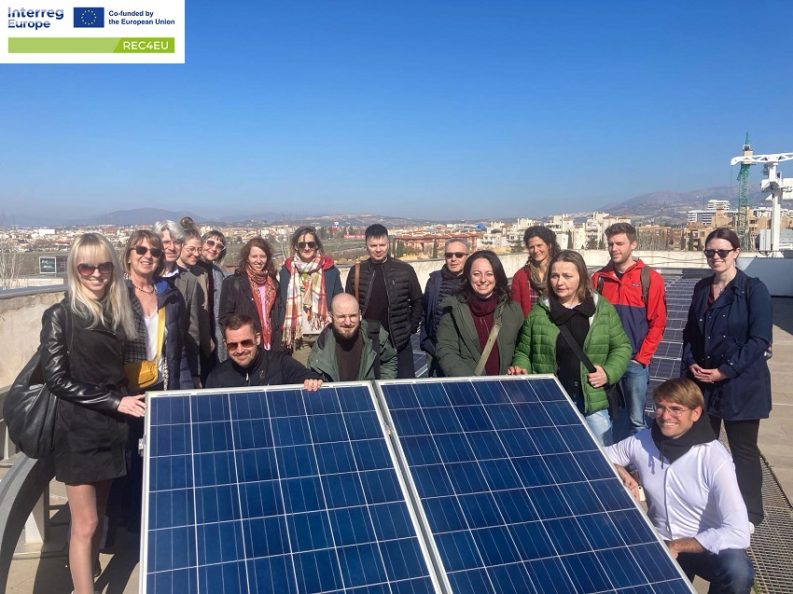 Uczestnicy spotkania w Hiszpnni, stoją na dachu budynku przy instalacji fotowoltaicznej.