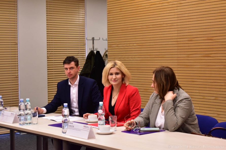 Dwie kobiety i jeden mężczyzna siedzą przy stole wewnątrz sali konferencyjnej