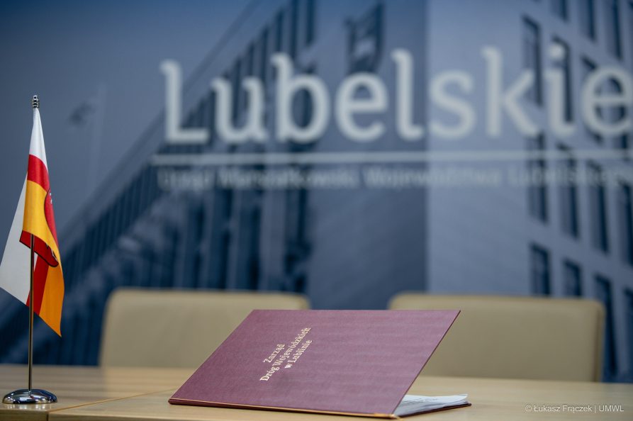 Teczka z napisem Zarząd Dróg Wojewódzkich która lezy na stole obok flagietek