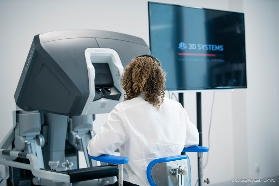 Kobieta w fartuchu lekarskim siedzi przy monitorze specjalistycznego sprzętu medycznego