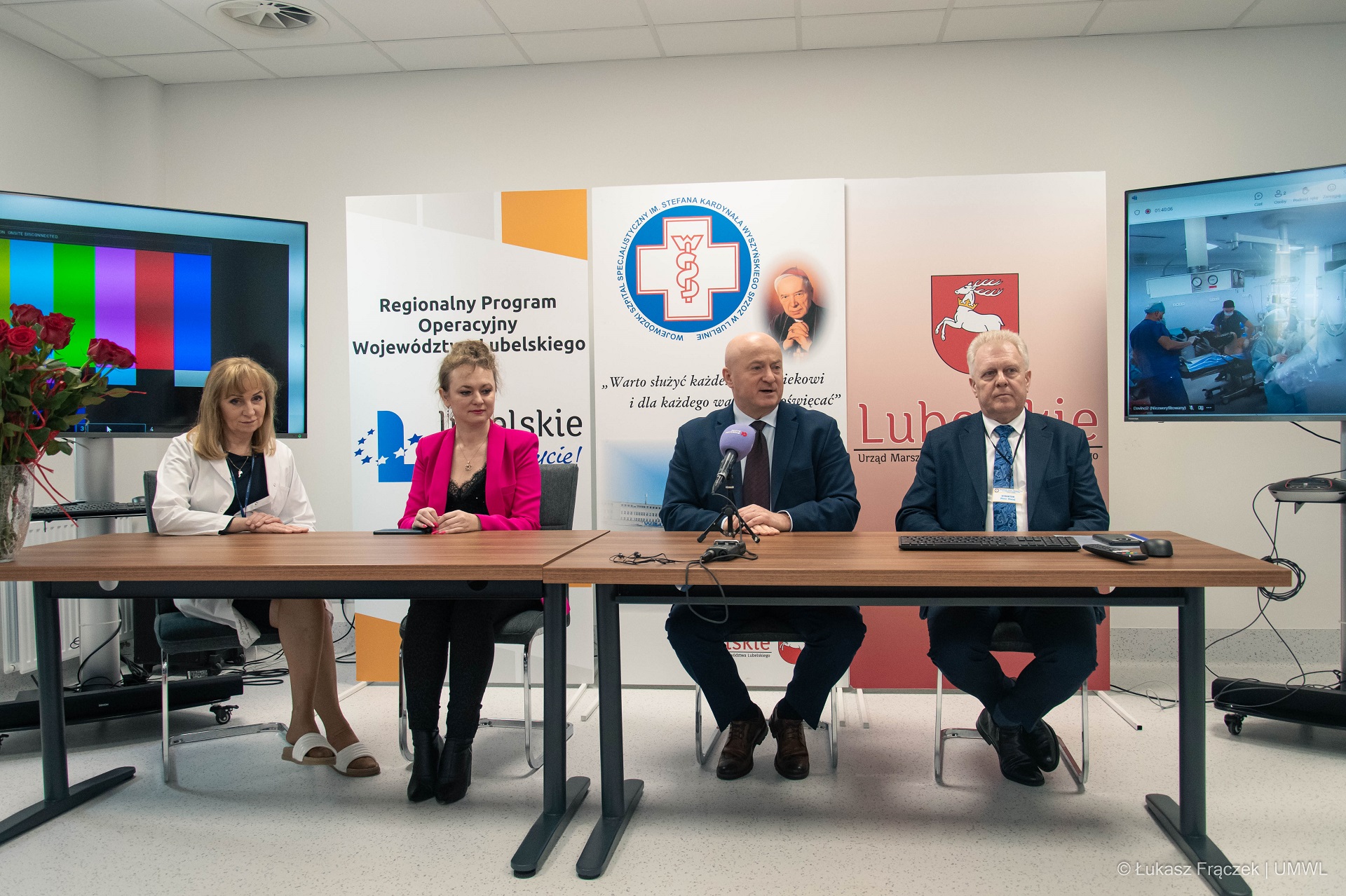 Cztery osoby, dwóch męzczyzn i dwie kobiety siedzą przy długim stole i biora udział w konferencji prasowej. Za nimi znadują się rollupy promocyjne dotyczące szpitala i fiuduszy europejskich