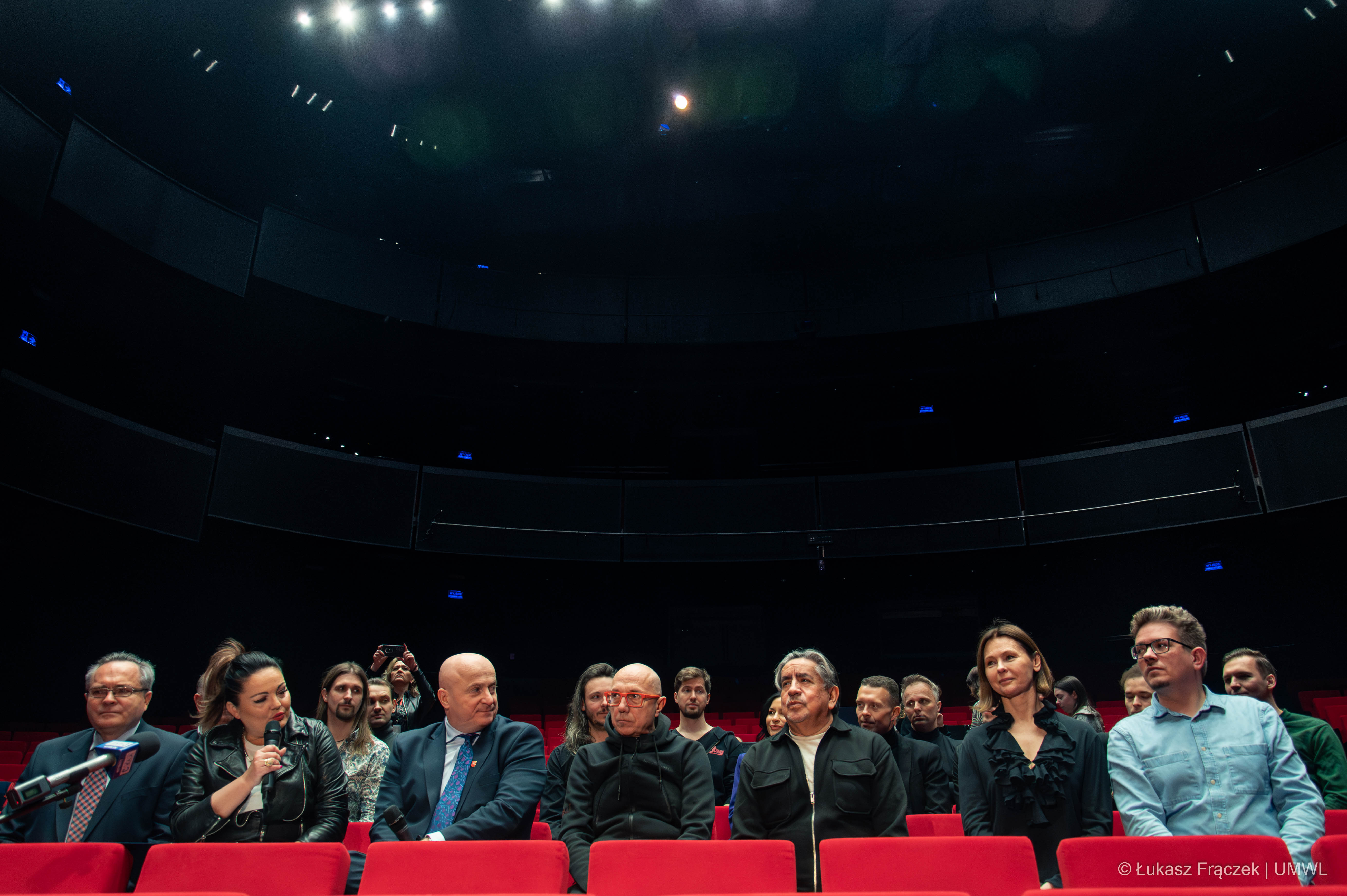 konferencja prasowa, która odbywa się w sali teatralnej. Na praktycznie pustej widowni siędzi około 12 osób, pracowników teatru, członów zarządu i aktorów. Jedna z osób trzyma mikrofon i udziela wypowiedzi.