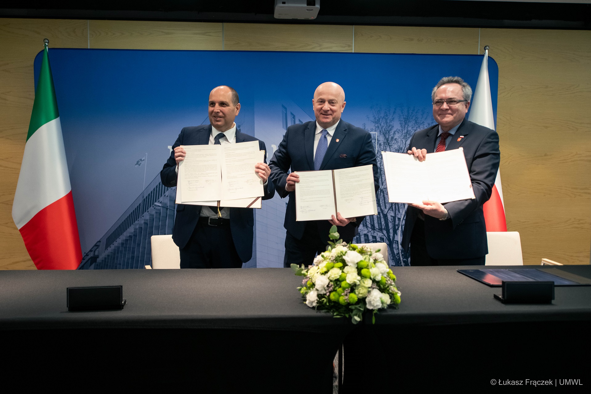 Marszałek i wicemarszałek województwa lubelskiego pozują do zdjęcia w towarzystwie przedstawiciela Lacjum. Każdy z nich trzyma w rękach otwartą tęczkę w której znjaduje się egzemplarz umowy o współpracy