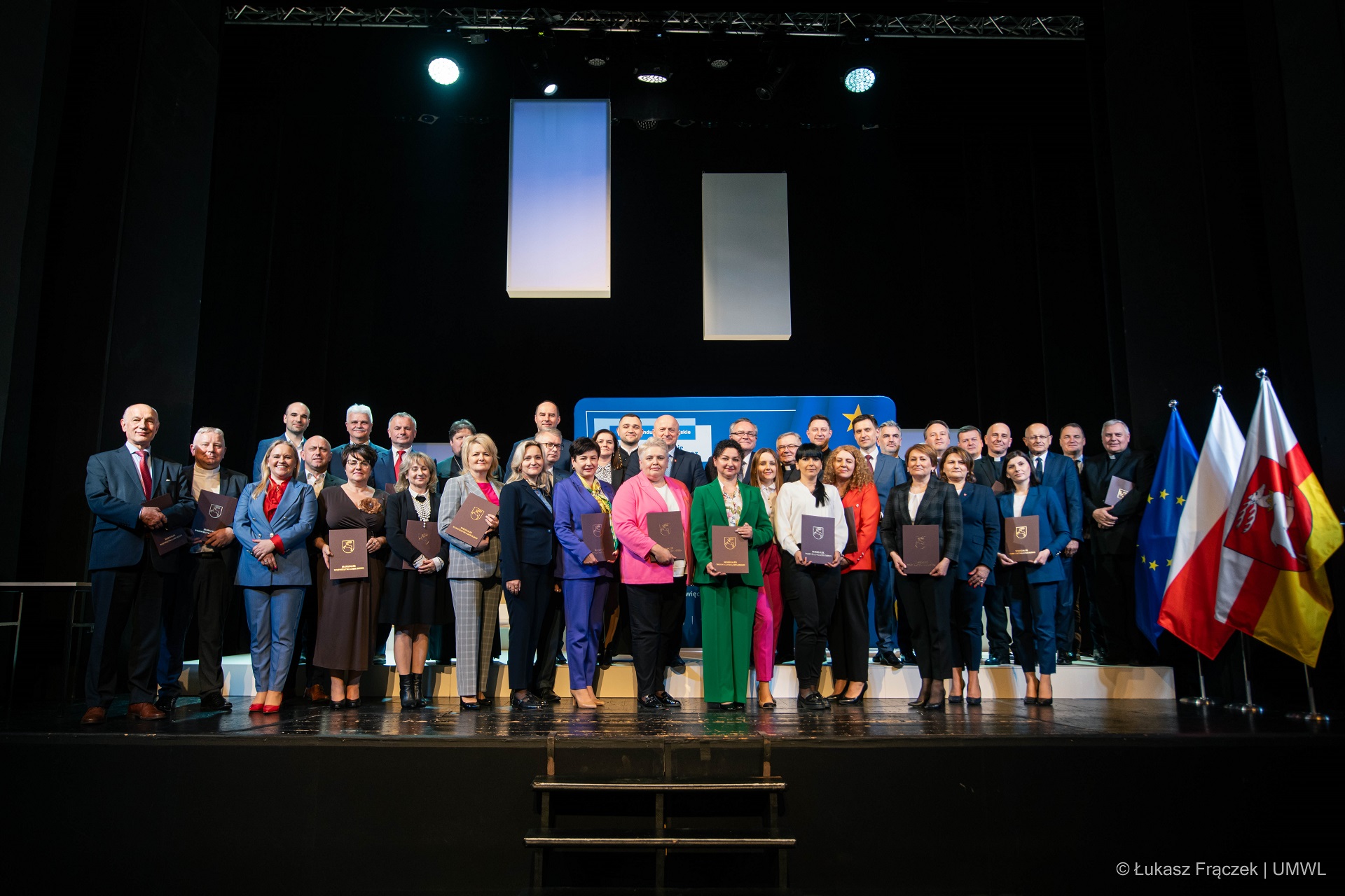 Na scenie teatralnej stoi około pięćdziesięciu osób. Wspólnie pozują do zdjęcia, są to beneficjenci funduszy europejskich w zakresie rozwoju dziedzictwa kulturowego