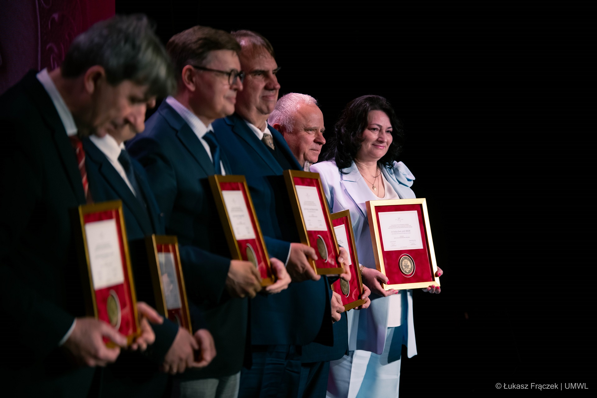 Czterech mężczyzn i jedna kobieta laureaci medalu, stoją na scenie i prezentują otrzymane medale, zdjęcie jest zrobione z profilu
