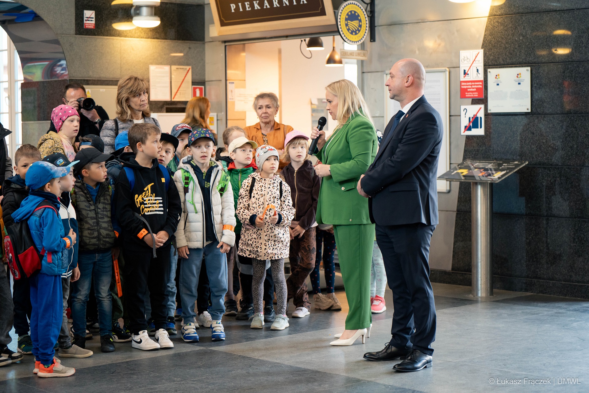 Wicemarszałek WL i Dyrektor Anna Brzyska stoją przed grupą dzieci w hali Dworca PKP