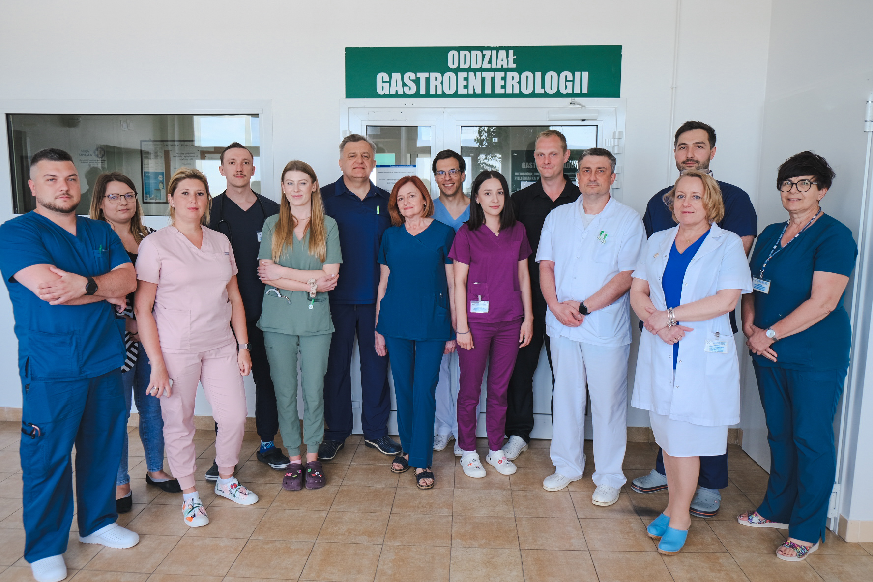 Około dziesięciu lekarzy i lekarek w fartuchach medycznych stoją na korytarzu przed drzwiami z napisem oddział gastroenterologii