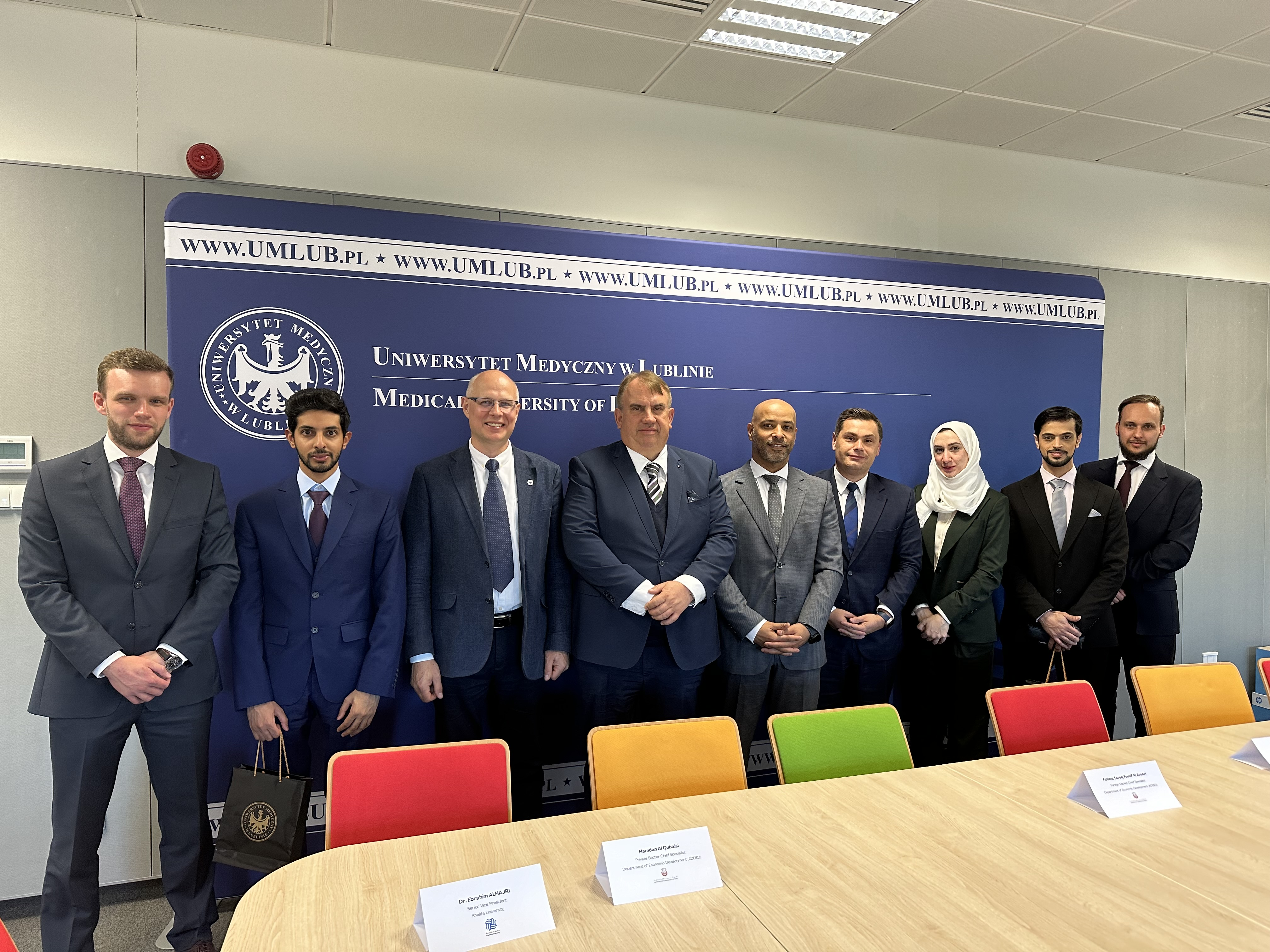 Około pięciu męzczyzn i jedna kobieta w burce pozują wspólnie do zdjęcia w malej sali konferencyjnej na tle ścianki Uniwersytetu Medycznego w