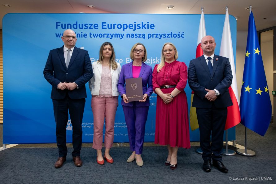 Trzy kobiety i dwóch mężczyzn pozują stojąc w jednej linii, za nimi znajduje się ściankapromocyjna dotycząca Funduszy europejskich