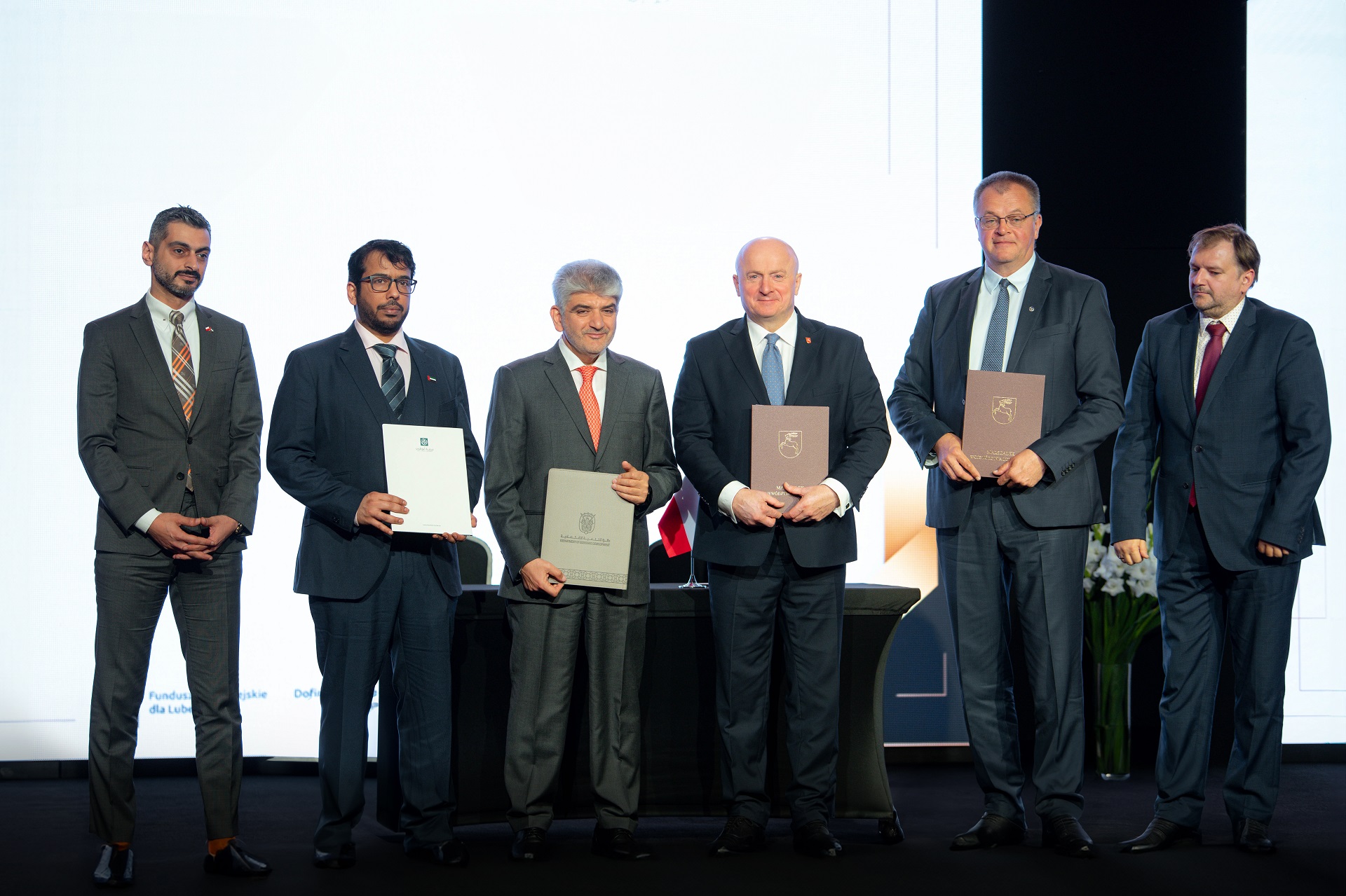 Marszałek WOjewództwa Lubelskiego wraz z pięcioma innymi mężczyznami w tym przedstawicielami kraju Abu Dhabi stoi na scenie i wspólne prezentują podpisane umowy