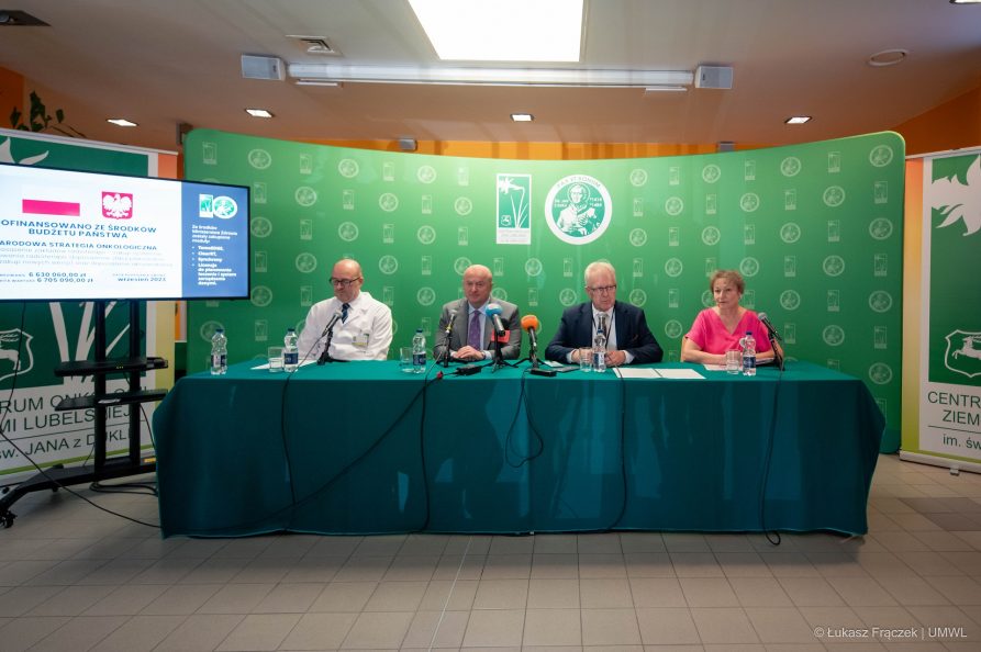 Trzech mężczyzn i jedna kobieta siedzą wspólnie przy stole konferencyjnym za nimi znajduje się ścianka