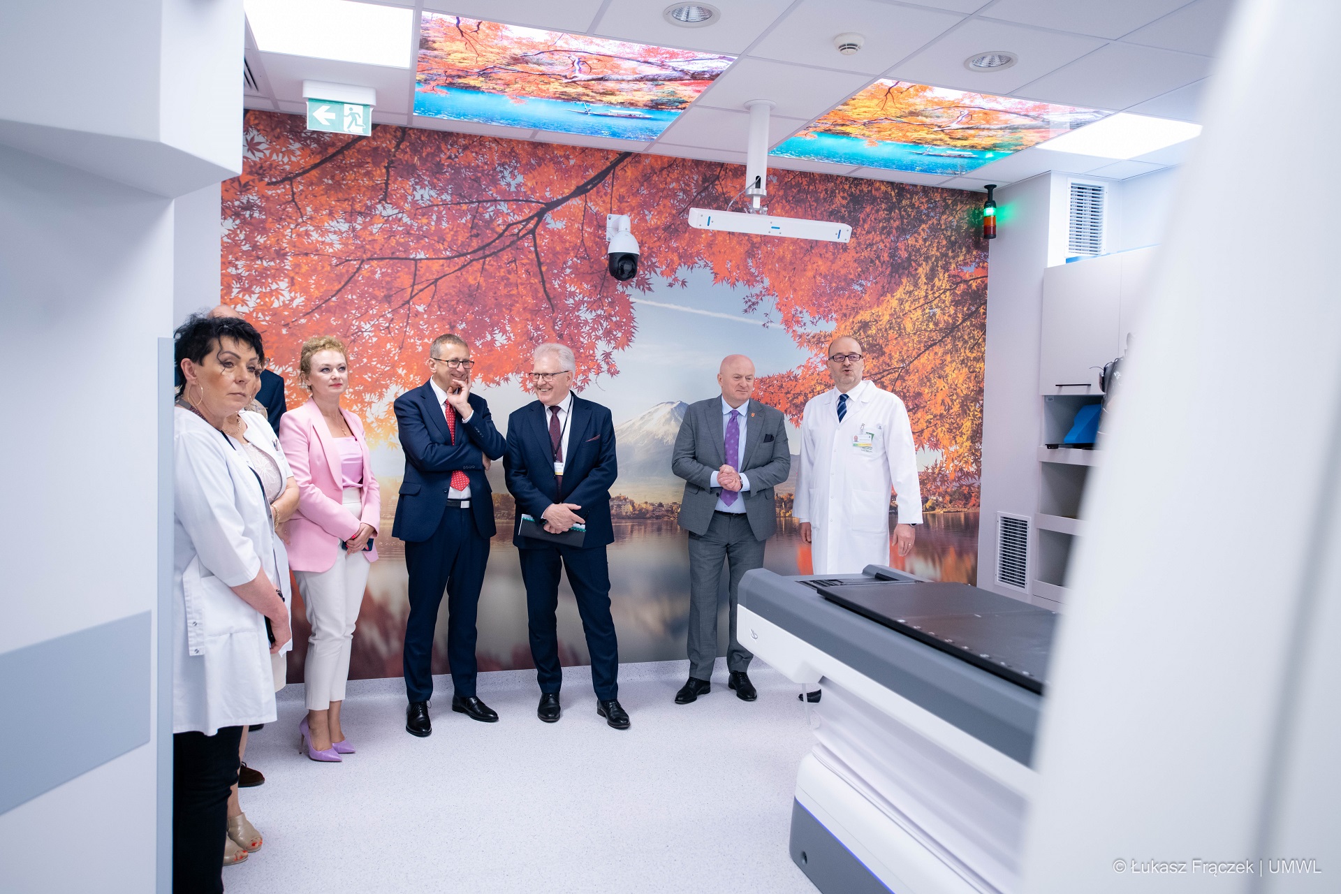 Kilkoro osób stoi w sali szpitalnej przy nowoczesnym aparacie do badania