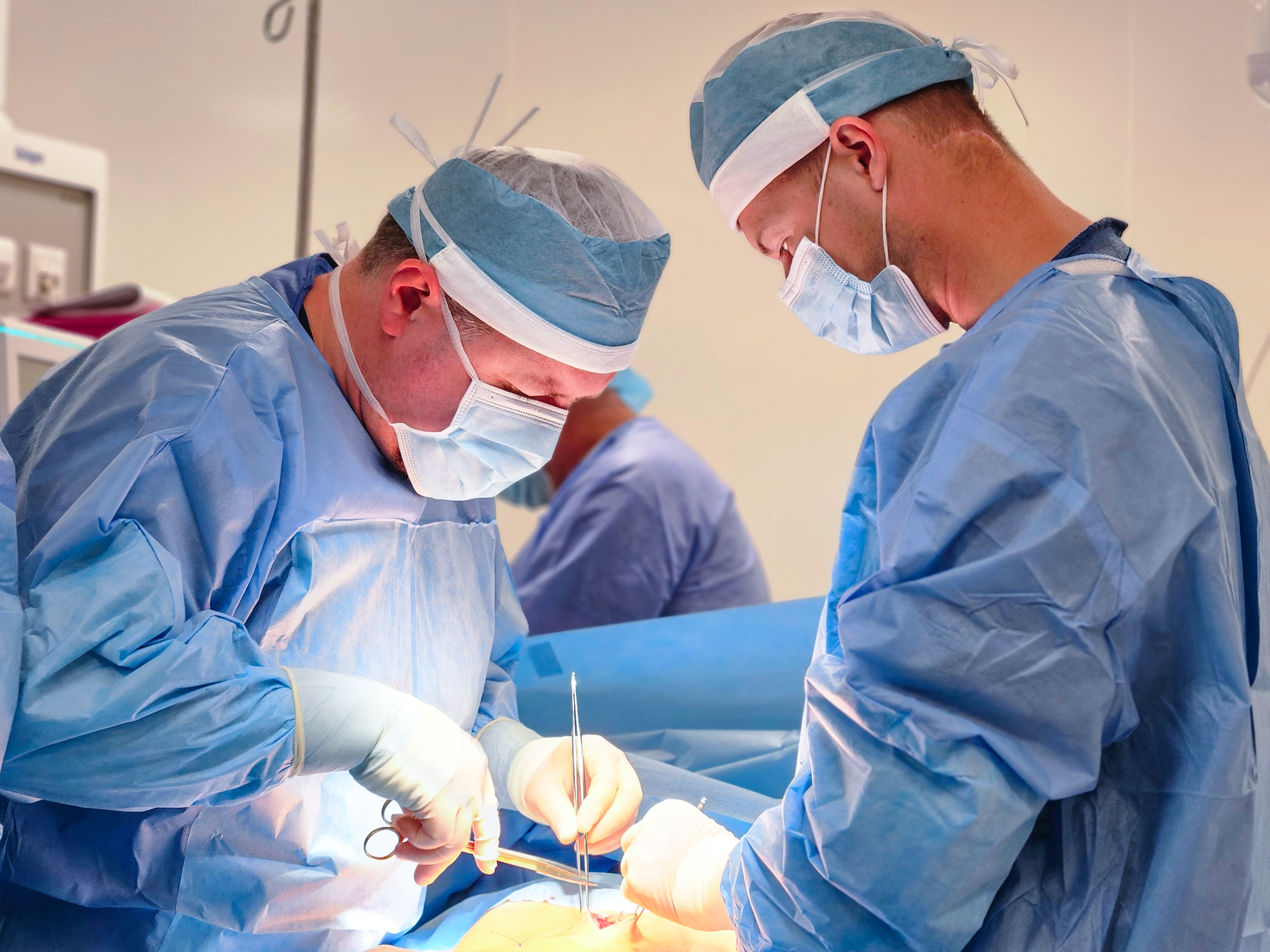 Dwóch chirurgów stoi pohcylonych nad stołem w czasie operacji