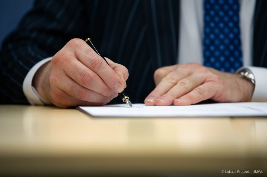 Męskie dłonie osoby, która podpisuje piórem dokument leżący na stole