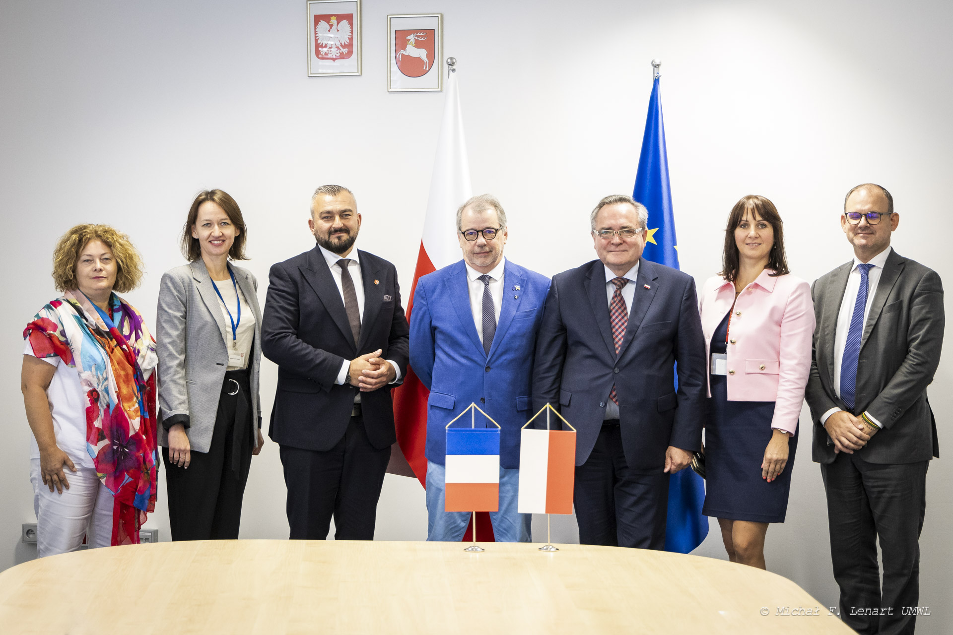 Trzech mężczyzn i dwie kobiety pozują wspólnie do zdjęcia w sali konferencyjnej, przed nimi na stole znajdują się dwie flagietki