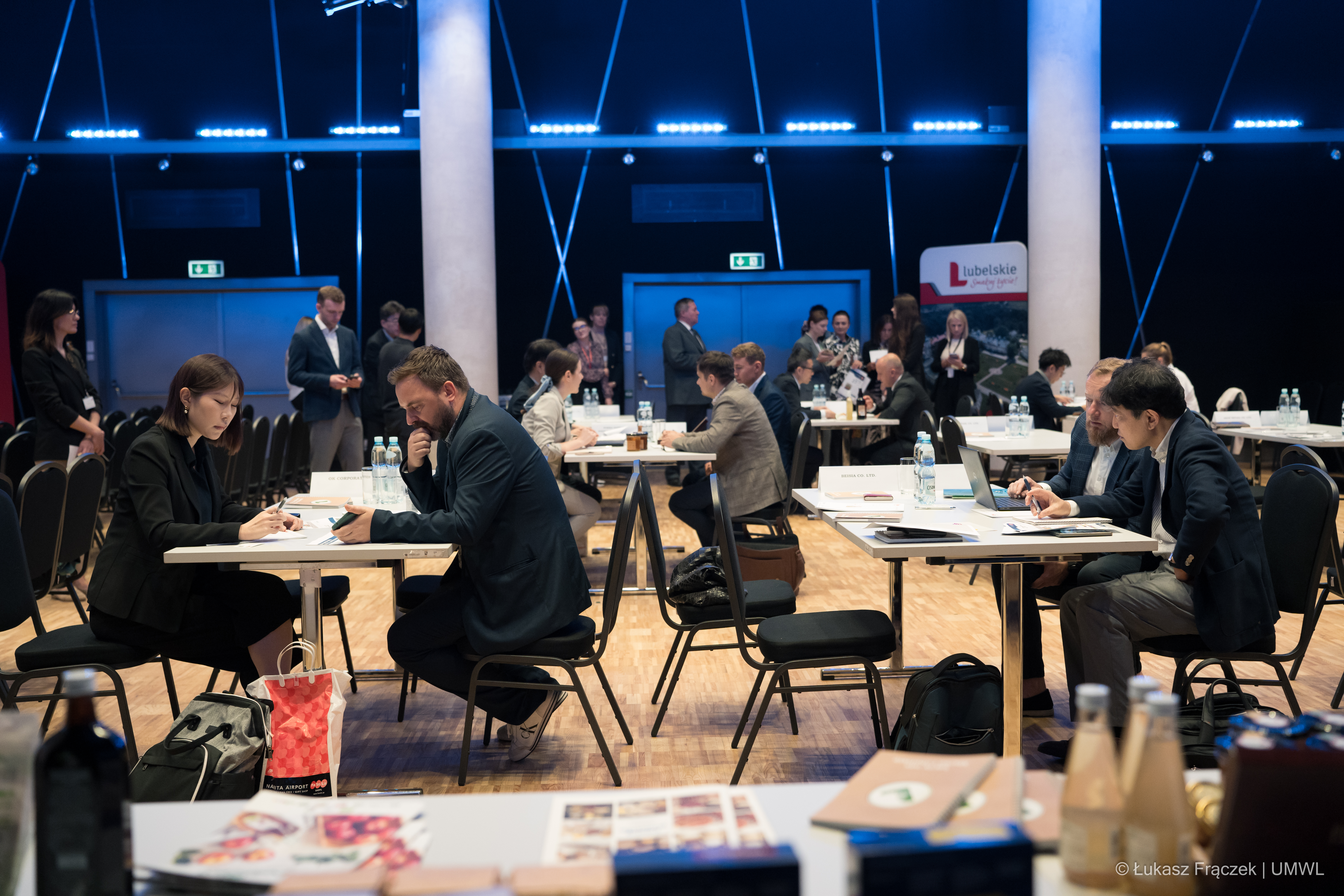 Na dużej sali konferencyjnej siedzi kilkanaście osób przy dwuosobowych stolikach i wspólnie rozmawiają