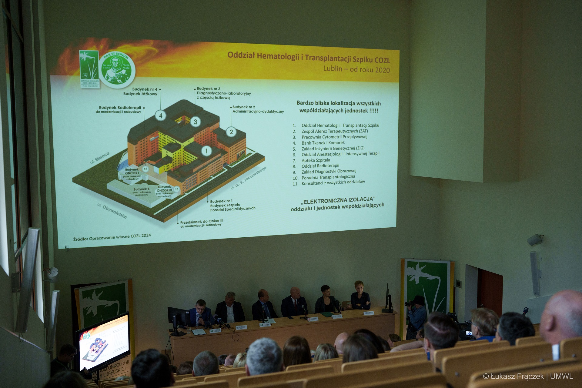 Na dużej sali konferencyjnej siedzi około dwudziestu osób, na ścianie widać duży slajd wyświetlający plany budowy nowego oddziału szpitalnego