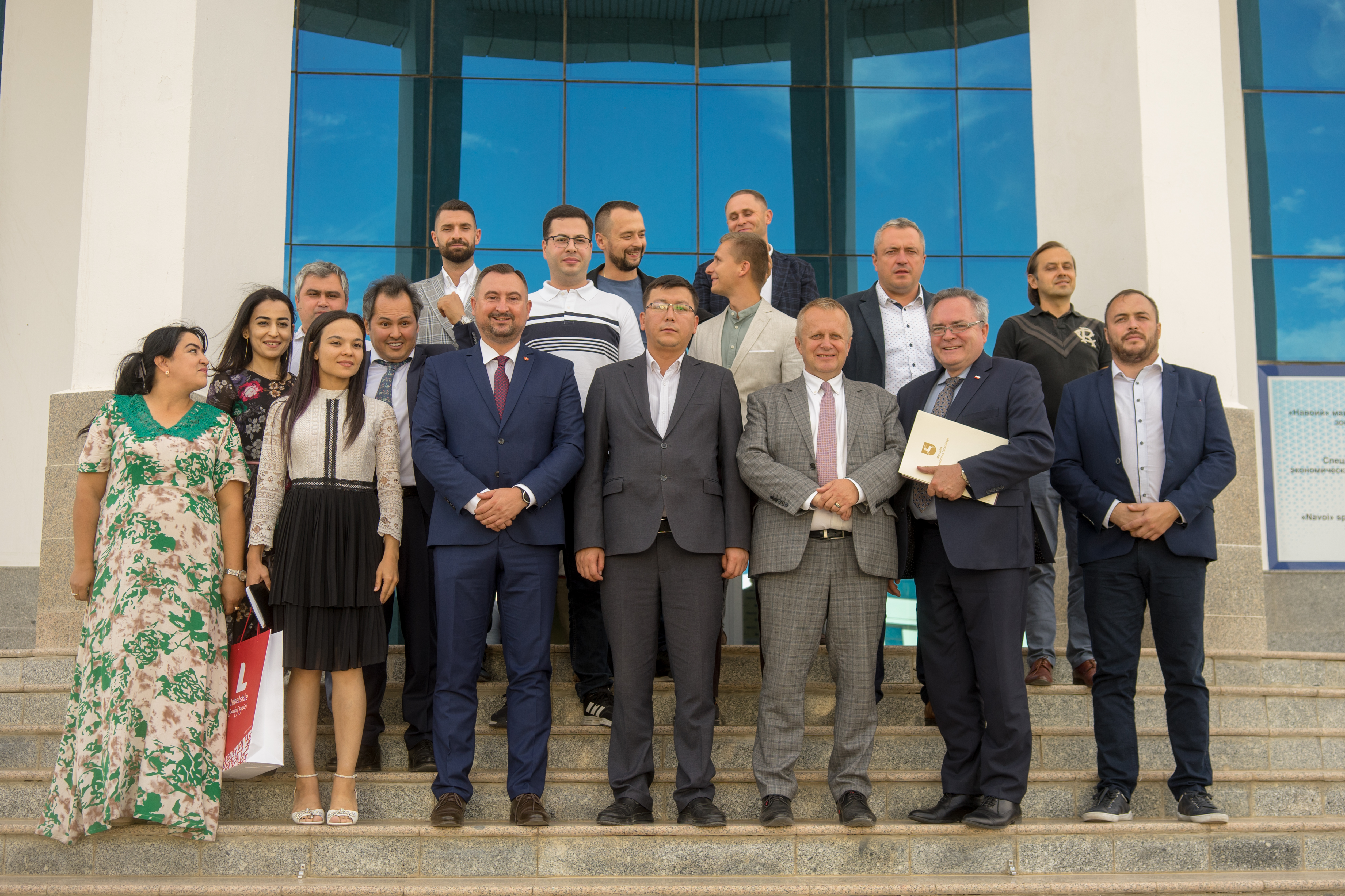 Grupowe zdjęcie okolo piętnastu osób, wszyscy stoją na schodach przed budynkiem i wspólnie pozują do zdjęcia