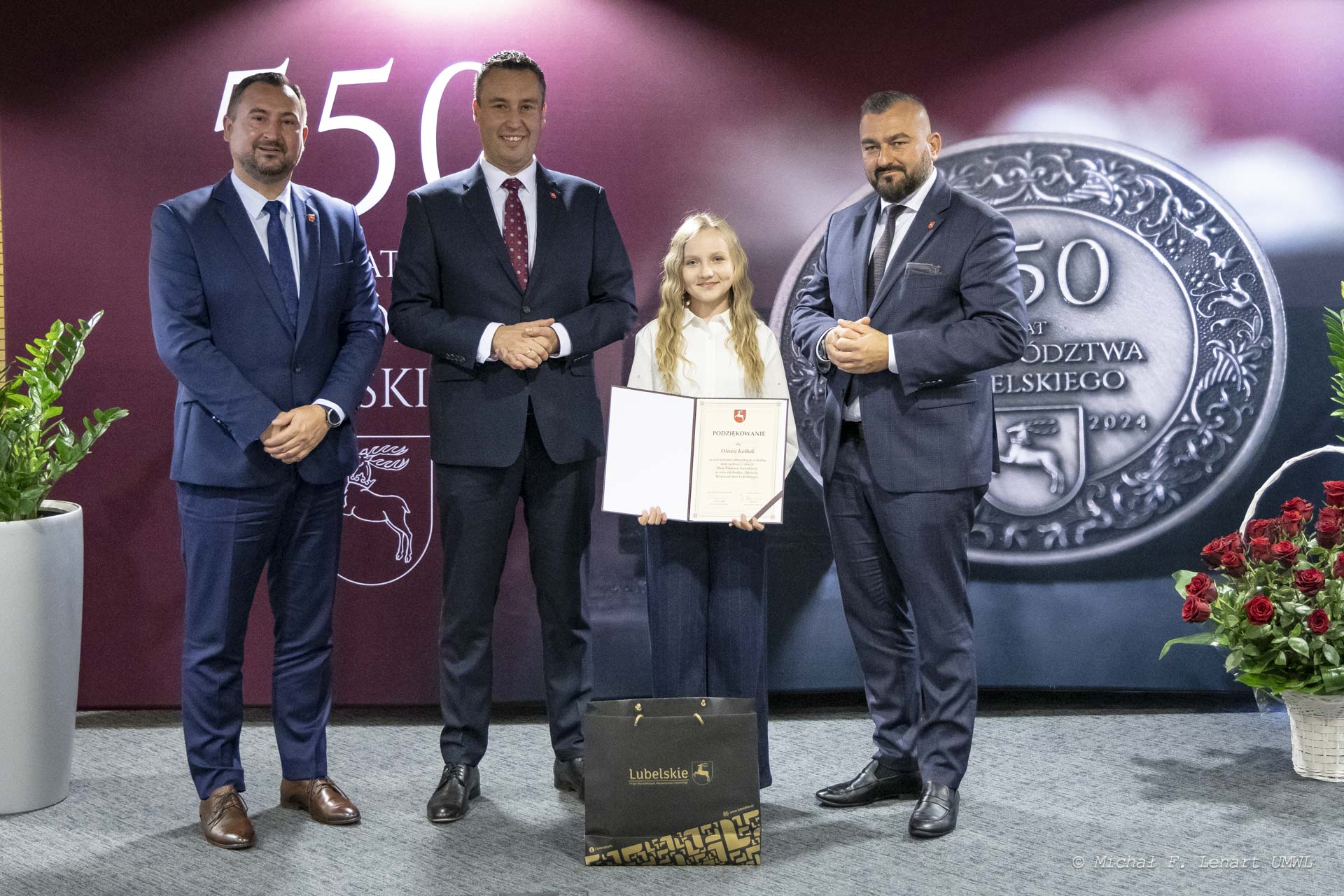 Członkowie Zarządu WL pozują do zdjęcia dziewczynką, która prezentuje otrzymany dyplom