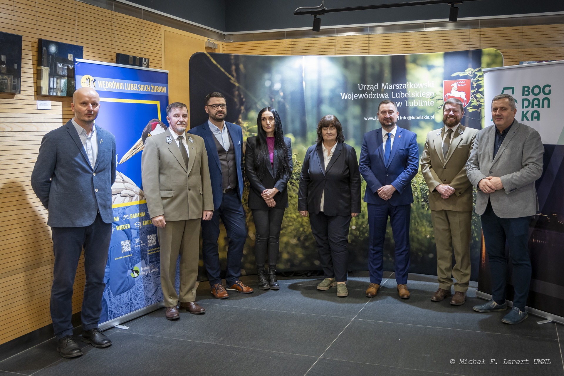 Wicemarszałek Marek Wojciechowski w towarzystwie około dziesięciu osób, wszyscy stoją na korytarzu na tle rollupów promocyjnych