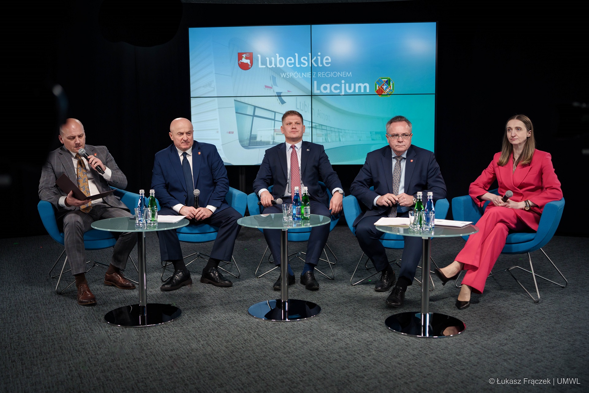 Na scenie zostało ustawionych pięć foteli na których siedzi czterech mężczyzn i jedna kobieta, za nimi na ekranie wyświetla się prezentacja