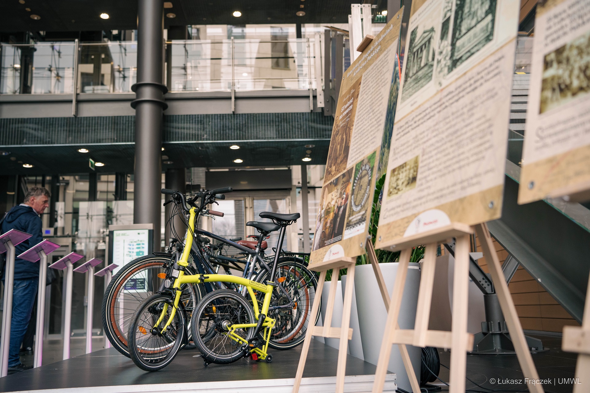 Na korytarzu stoi wystawa zdjęć wraz z ustawionymi rowerami