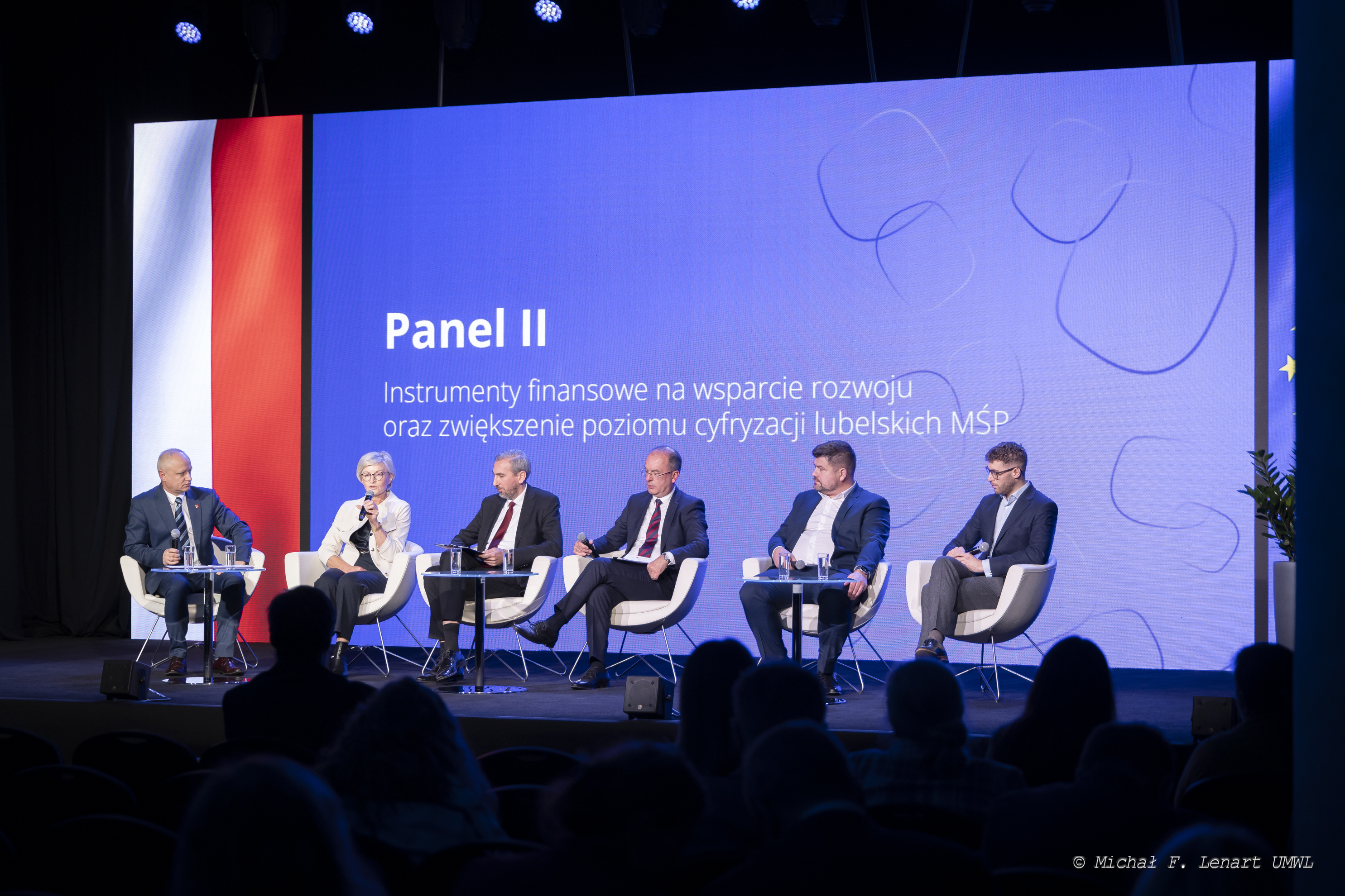 Sześciu uczestników panelu siedzia na fotelach ustawionych na scenie. Za nimi na dużym ekranie wyświetla się tytuł panelu