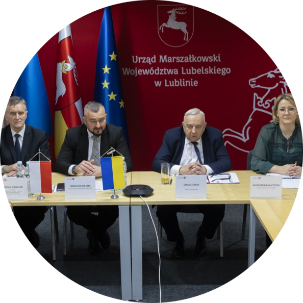 Uczestnicy spotkania poświęconego nawiązaniu partnerskiej współpracy samorządów na tle flag i herbu Województwa Lubelskiego.