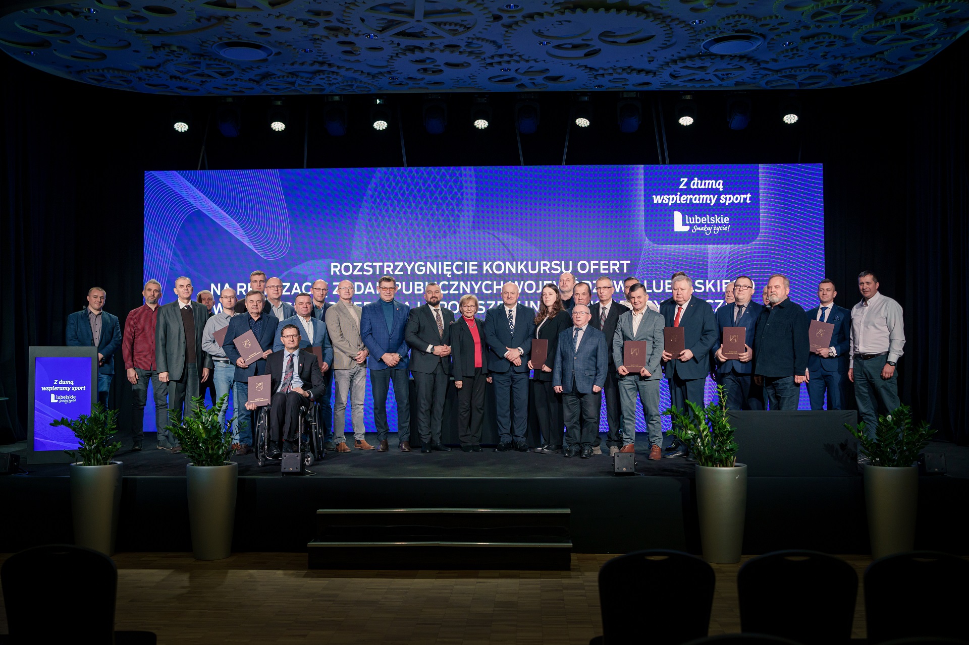 Wspólne zdjęcie beneficjentów programu, łącznie około dwudziestu osób stoi na scenie w towarzystwie marszałka województwa lubelskiego