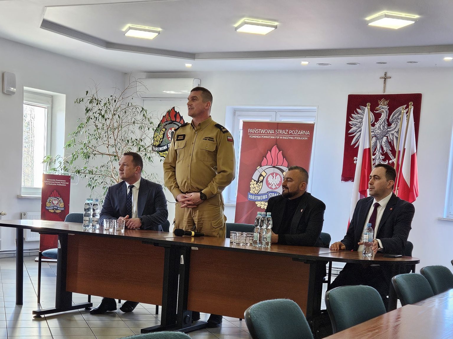 Czterech mężczyzn przy stole prezydialnym. Jeden stoi i mówi