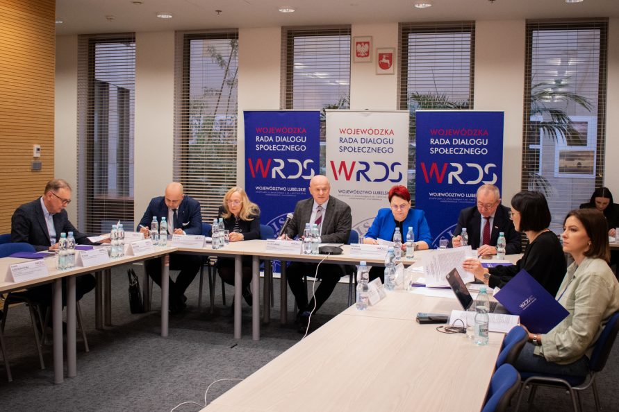 Spotkanie Wojewódzkiej Rady Dialogu Społecznego w województwie Lubelskim. Przy stole siedzą uczestnicy obrad, analizując tematy posiedzenia. Centralną postacią jest przewodniczący WRDS WL, Jarosław Stawiarski, Marszałek Województwa Lubelskiego, który prowadzi posiedzenie.