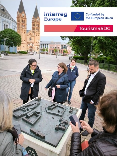 Uczestnicy spotkania oglądają miniaturę budynku historycznego stojąc w plenerze.