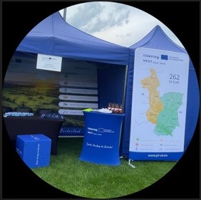 Widok stoiska Regionalnego Punktu Programu, składającego się z niebieskich namiotów, pufów, stoliczków i ścianek dekoracyjno - informacyjnych.
