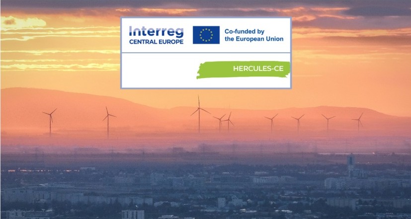 Farma wiatraków na tle zachodu słońca z logiem projektu HERCULES-CE w prawym górnym rogu