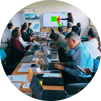 Partnerzy projektu pracują razem przy stole, słuchając prezentacji