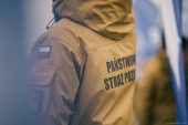 Strażak stojący w kurtce z napisem Państwowa Straż Pożarna