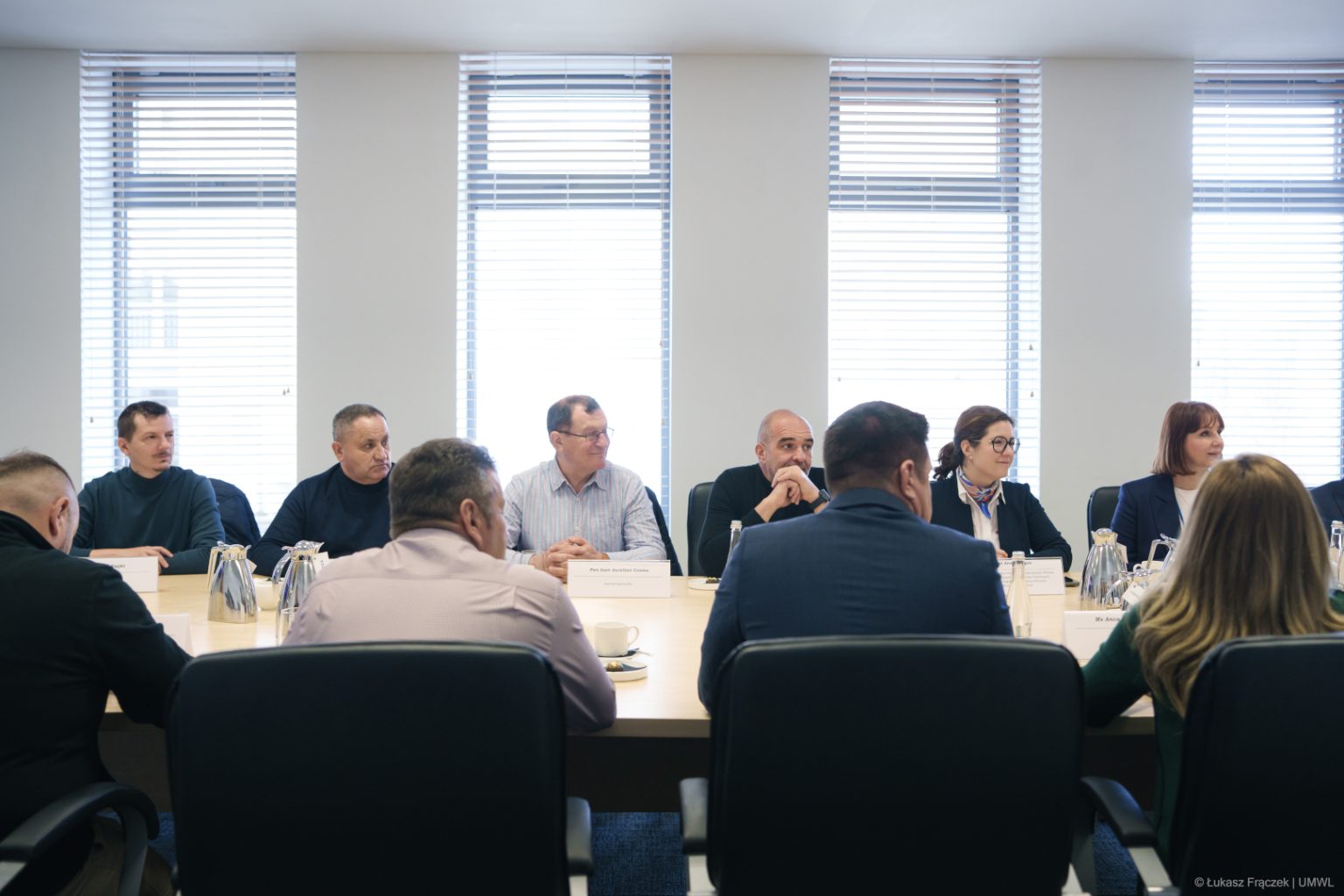 Delegacja siedzi przy stole w sali i uczestniczy w spotkaniu.