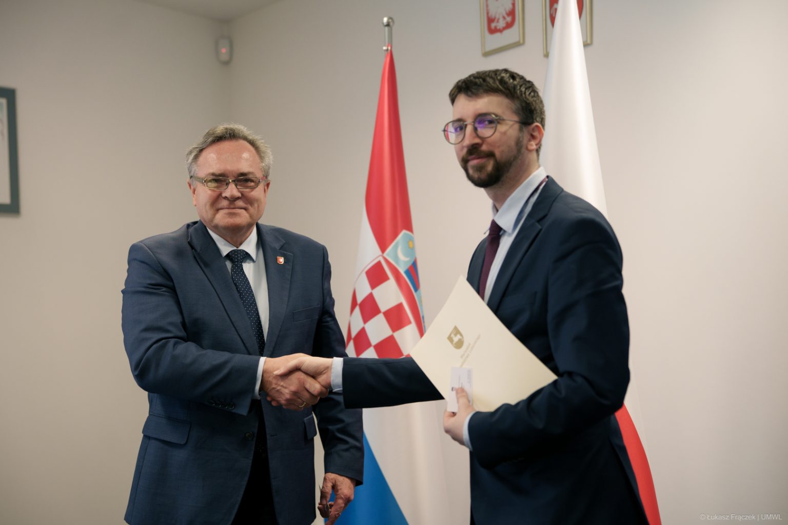 Przewodniczący Komisji Pan Zbigniew Wojciechowski i Pierwszy Sekretarz Ambasady Chorwacji w Polsce Pan Lucio Borčić podaj sobie ręce. W tle widać flagi państwowe Polski oraz Chorwacji.