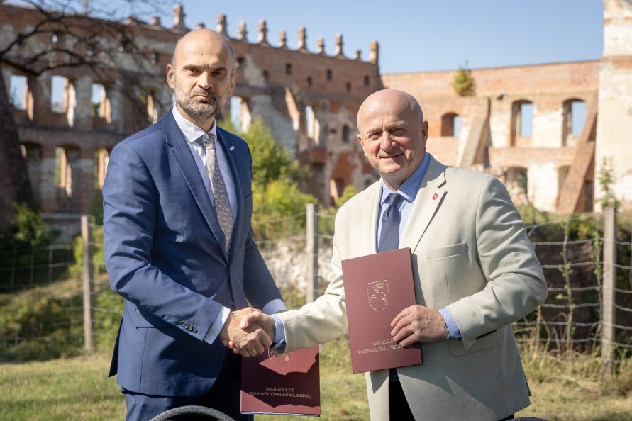 Marszałek Stawiarski pozuje do wspólnego zdjęcia z beneficjentem. W tle mury zamku.