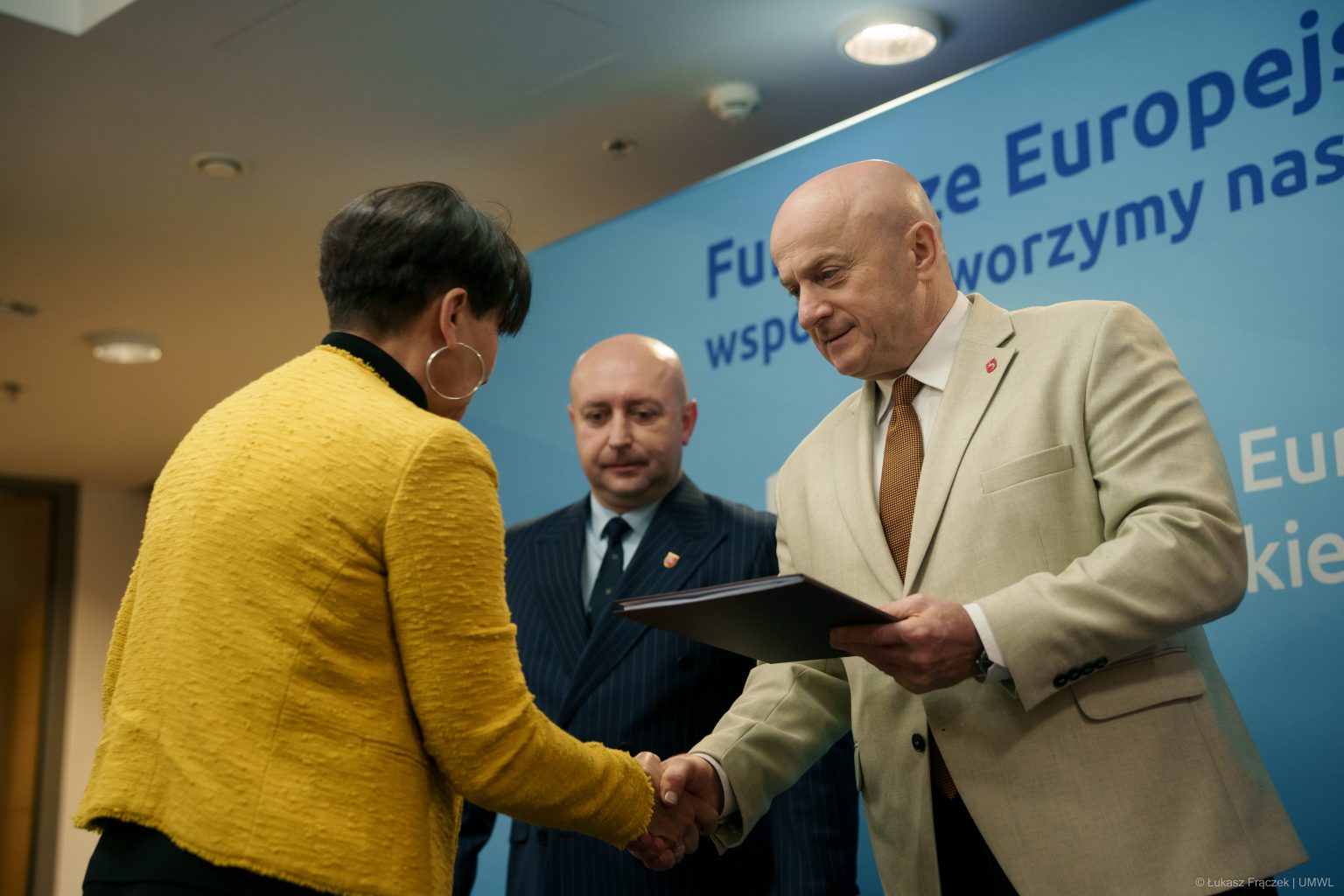 Marszałek Stawiarski oraz Wicemarszałek Breś wręczają beneficjentce teczkę.