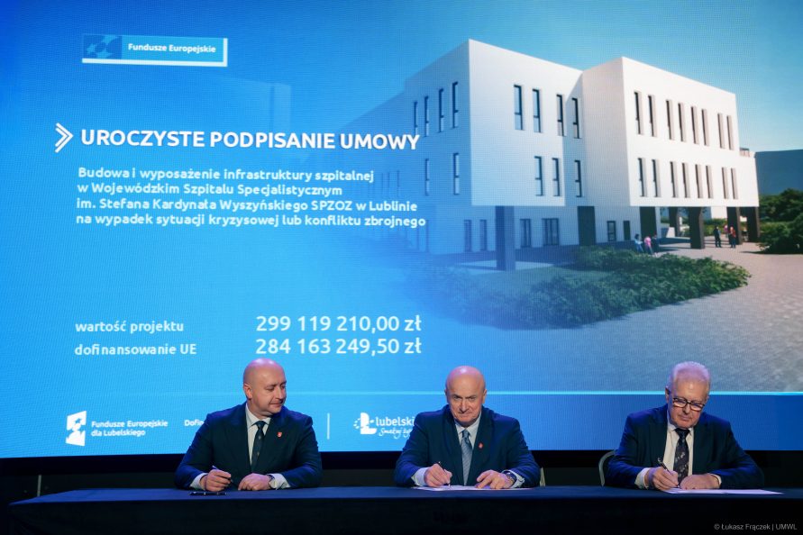 Trzech mężczyzn siedzących przy wspólnym stoliku i podpisujący dokumenty. Wśród nich między innymi Jarosław Stawiarski.
