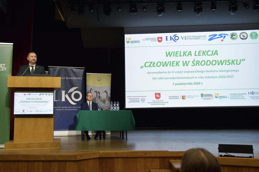 Scena auli z prelegentem przy trybunce. W tle ekran z nazwą wydarzenia "WIELKA LEKCJA CZŁOWIEK W ŚRODOWISKU" wraz z logo organizatorów i partnerów. Poniżej banery organizatorów.